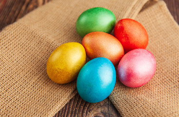 Obraz na płótnie Canvas Colored easter eggs on a wooden background on burlap, top view