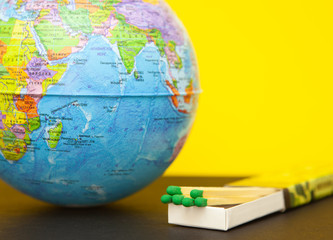 Matchstick and world globe on a yellow background, concept of saving the planet from fire