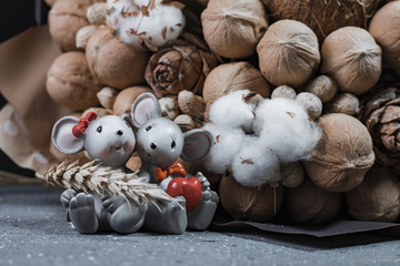 Fototapeta na wymiar Statuette of two mice in love with Bouquet of various nuts with branches of cotton plant and ears of rye. Coconut, pine nut, walnut, peanut.