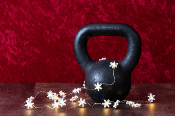 Fototapeta na wymiar Holiday fitness, black kettlebell with white snowflake twinkle lights, against a red background
