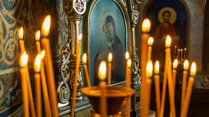 Blurred wax burning candles in an orthodox church on the icon background. - obrazy, fototapety, plakaty