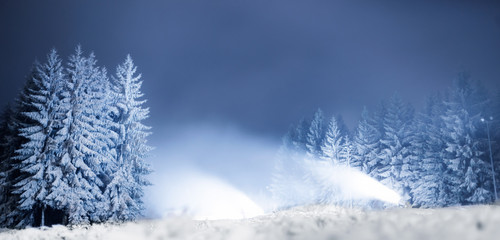 Snow cannons at night on a forest road in the background of snowy trees
