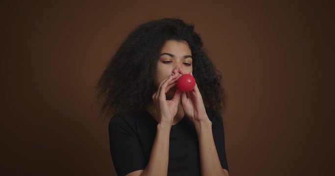 Portrait of african american girl inflates a red balloon at brown background