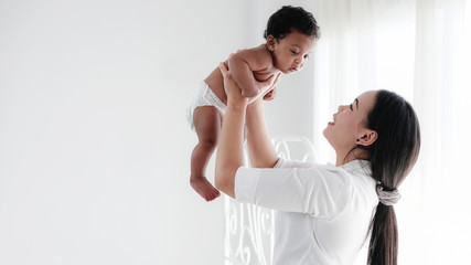 portrait of asian mother and her black mixed race baby girl in white room