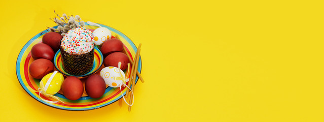 happy Easter. Greeting Easter background with a plate, painted Easter eggs and willow twigs. Concept of Easter banner greeting card on a bright yellow background top view.