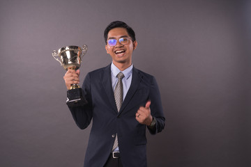 Happy young male intrepreneur or business man holding his gold trophy and celebrating his victory.Studio shot.