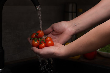 Men's hands are holding branch of tomatos in water jet. Product preparation for home cooking at summer. Shallow depth of field.