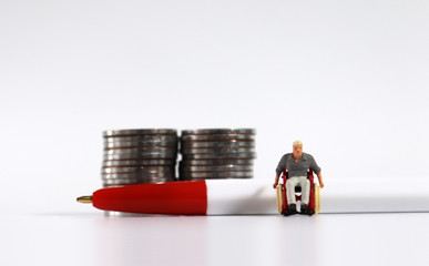 A miniature man in a wheelchair with a red ballpoint pen in front of a pile of coins.
