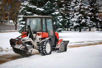 Tractor cleaning sidewalk from snow with snow plow and rotating brush. Municipal service removing...