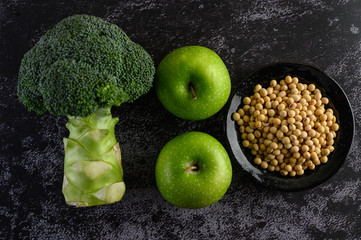 Broccoli, Apple, and soy beans on a black cement floor background.