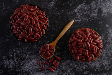 Red beans in a wooden bowl and wooden spoon on the black cement floor.