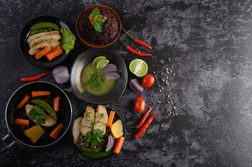 Assorted food and dishes of vegetables, meat and fish on a black stone background. Top view.