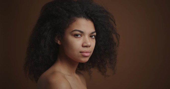 Profile portrait of nude african american girl looking to camera brown backdrop