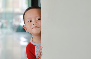 Little Asian baby boy hide behind a corner room. Small children playing peekaboo game indoor.