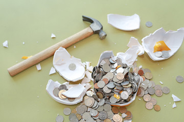 Broken piggy bank with hammer and coins on table.