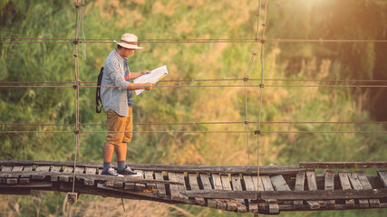 Obraz na płótnie Canvas Asian tourist man walking on the old and broken wood bridge