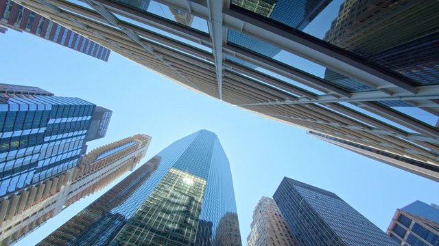 Low angle pan view on New York City corporate skyscrapers with mirroring glass facades, clear blue sky sunny day