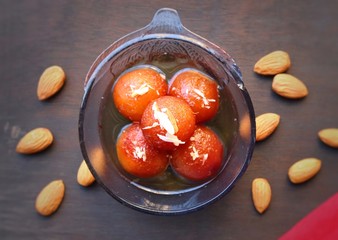 Gulab Jamun in a glass bowl on wood background with Almonds