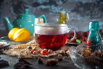 Red Hot Hibiscus tea in a glass mug on a wooden table among rose petals and dry tea custard with metallic heart