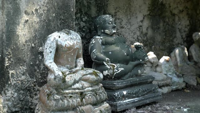 Stone statues of Fat Buddha and headless Buddhist figure in meditation