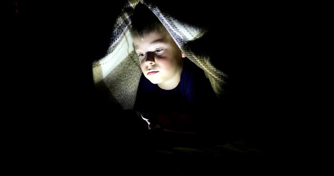 Little boy watching content on her smartphone. The pitfalls of social networks. The childern secretly communicates over the Internet at night. Viewing inappropriate content.