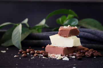 Stacked pieces of milk chocolate and white chocolate bar on black background with coffee beans.