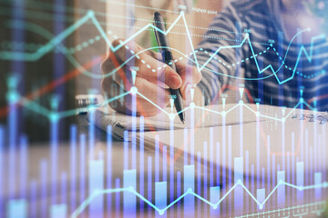 Financial forex graph drawn over hands taking notes background. Concept of research. Double exposure
