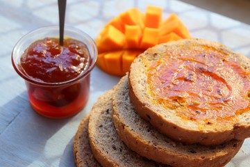 Nutritious Breakfast of fresh multigrain bread and mango jam with a slice of fresh mango on a wooden plank