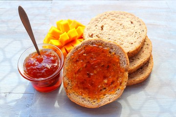 Nutritious Breakfast of fresh multigrain bread and mango jam with a slice of fresh mango on a wooden plank