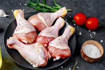 raw chicken legs with spices on a black plate on a stone background