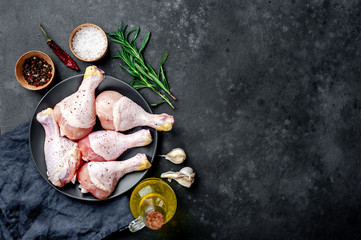 raw chicken legs with spices on a black plate on a stone background with copy space for your text