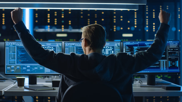 IT Specialist Working on Personal Computer with Monitors Showing Coding Language Program, He Celebrates His Success by Doing YES Gesture. Technical Room of Data Center.