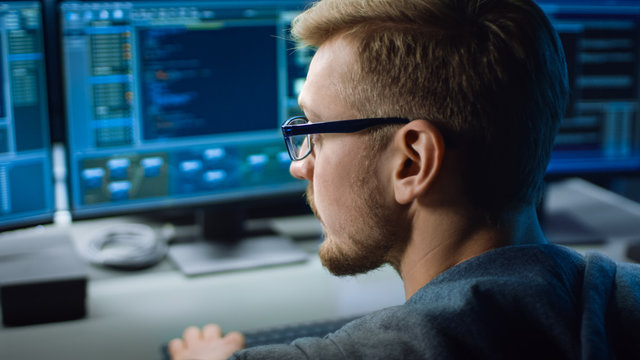 IT Specialist Works on Personal Computer with Screens Showing Software Program with Coding Language Interface. In the Background Technical Room of Data Center with Professional Working
