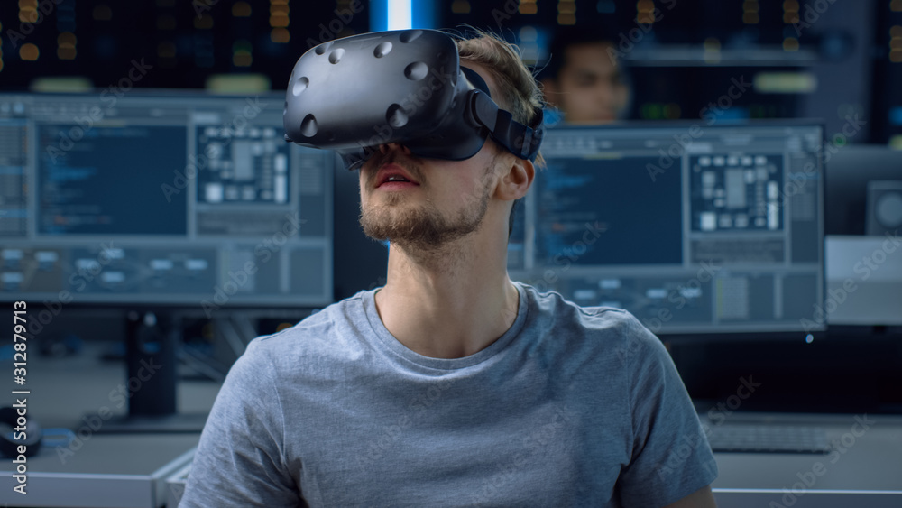 Fototapete Software Delevoper Wearing Virtual Reality Headset Gesturing with His Head, Developing and Programming VR Game or Application. In Background Technology Developing Studio with Computers and Monitors