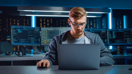 Portrait of Software Developer / Hacker Wearing Glasses Sitting at His Desk and Working on Computer in Digital Identity Cyber Security Data Center. Hacking or Programming.