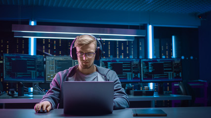 Portrait of Software Developer / Hacker / Gamer Wearing Glasses and Headset Sitting at His Desk and...