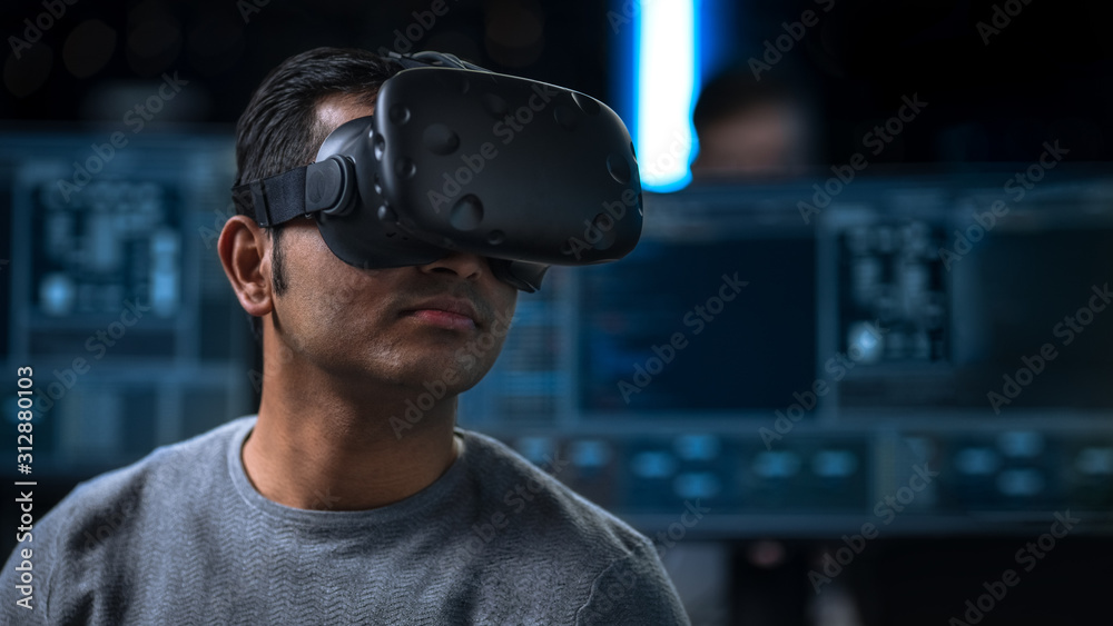 Fototapete Software Delevoper Wearing Virtual Reality Headset on His Head, Developing and Programming VR Game or Application. In the Background Technology Developing Studio with Computers and Monitors