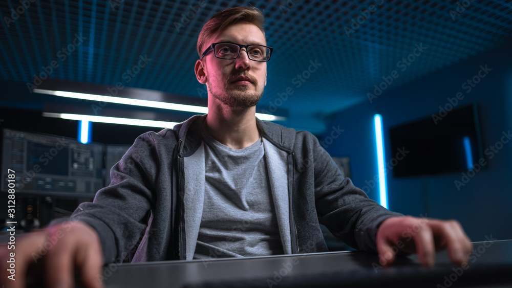 Aufkleber Low Angle Portrait Shot of Software Developer / Hacker Wearing Glasses Sitting at His Desk and Working on Computer in Digital Identity Cyber Security Data Center. Hacking or Programming.