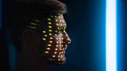 Handsome Young Caucasian Man is Identified by Biometric Facial Recognition Scanning Process. Futuristic Concept: Projector Identifies Individual by Illuminating Face by Colorful Dots and Laser