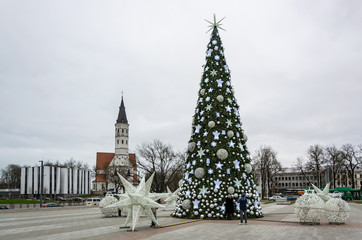 Fototapeta na wymiar Siauliai, Lithuania - A Christmas tree in the square decorated with white balls, angels, stars and snowflakes, next to it are white installations of balls and stars, in the background is the cathedral