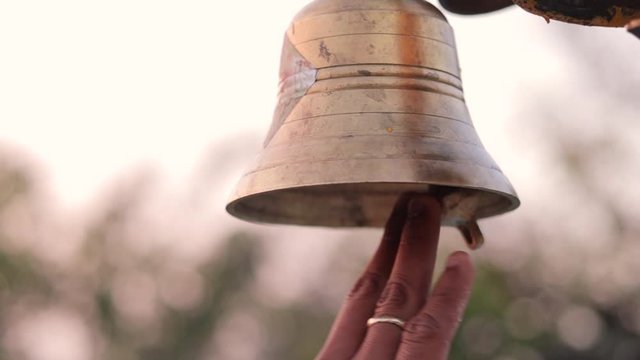Close up of hands ringing bell at temple sanctum during puja or worship.