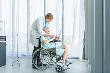 Fototapeta premium Doctor Pushing Patient In Wheelchair Along Corridor