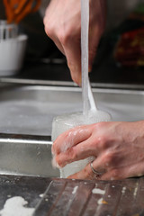 Doing dishes after cooking at home. Caucasian male doing the dishes. Closeup image. In this photo there is a transparent box being washed with a lot of soup bubbles and running water. Color image.