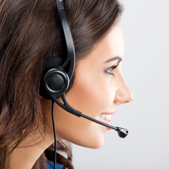 Portrait of smiling female support phone operator or sales agent in headset, over grey background....