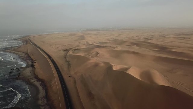 4K aerial revealing drone video of Namibian Atlantic Ocean coastline, enormous sand dunes panorama, seascape, waves along highway road between Swakopmund and Walvis Bay harbour, west coast, Namibia