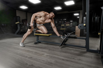 Fototapeta na wymiar Muscular strong athletic bodybuilder doing one-arm dumbbell rows on bench in gym. Concept sport photo with copy space