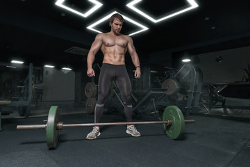 Fototapeta na wymiar Muscular strong athletic guy without shirt looking at the barbell, workout in the gym