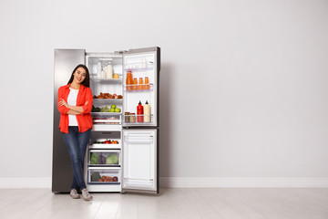 Happy young woman near open refrigerator indoors, space for text