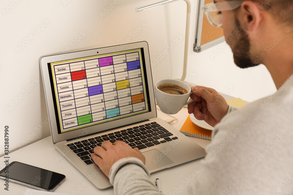 Wall mural Young man using calendar app on laptop in office, closeup