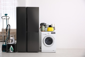 Refrigerator and different household appliances in room. Space for text